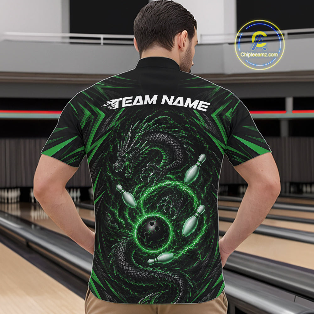 A man viewed from behind wearing a black short-sleeve bowling shirt with a green dragon and bowling pins graphic on the back, standing in a bowling alley. The shirt has 'TEAM NAME' printed across the upper back.