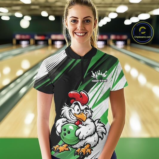 A woman wearing a custom bowling shirt with a cartoon rooster holding a bowling ball, set against a blurred bowling alley background. The shirt features green, black, white, and red colors with a custom name printed on the chest.