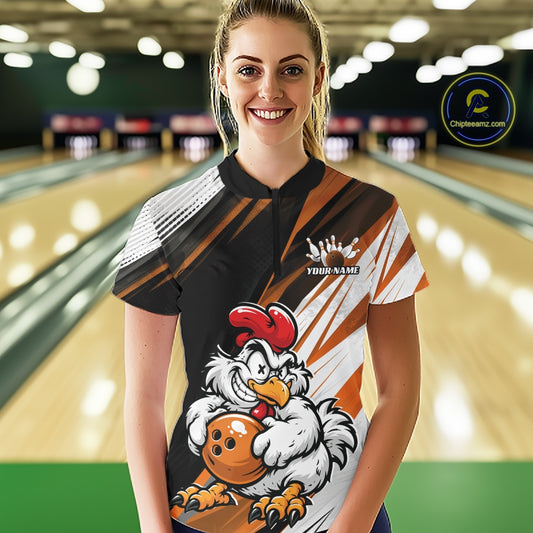 A woman standing in a bowling alley wearing a custom short-sleeve bowling shirt with a cartoon chicken graphic holding a bowling ball. The shirt features a black, white, and orange diagonal striped pattern with a white customizable name graphic on the chest.