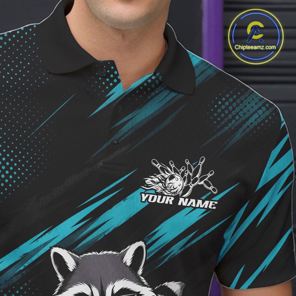 A close-up of a person wearing a black polo shirt with teal diagonal brushstroke graphics, a white raccoon graphic, and a customizable chest print reading 'YOUR NAME.' 