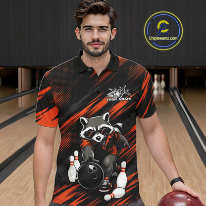 A man wearing a black and orange bowling-themed polo shirt with a raccoon graphic, standing in a bowling alley holding a bowling ball. 
