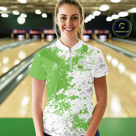 Front view of a female model in a bowling lane wearing a green and white splatter bowling quarter-zip shirt with minimalist bowling-themed design accents.