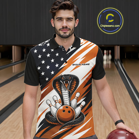 A smiling man stands in a bowling alley wearing a black, white, and orange bowling shirt with stars, diagonal stripes, a cobra, pins, and an orange ball.