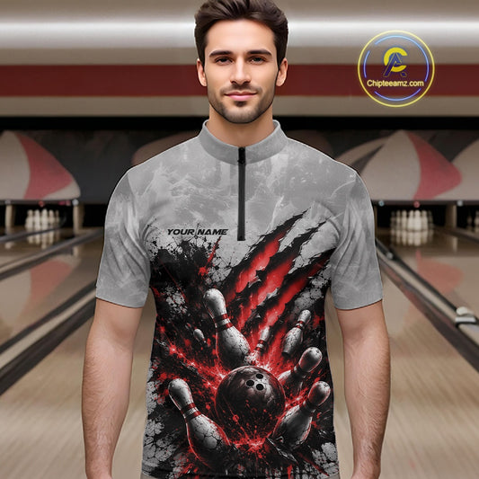 Male model wearing a gray bowling quarter zip shirt with a dramatic red bowling ball striking pins graphic, shown from the front in a bowling lane.
