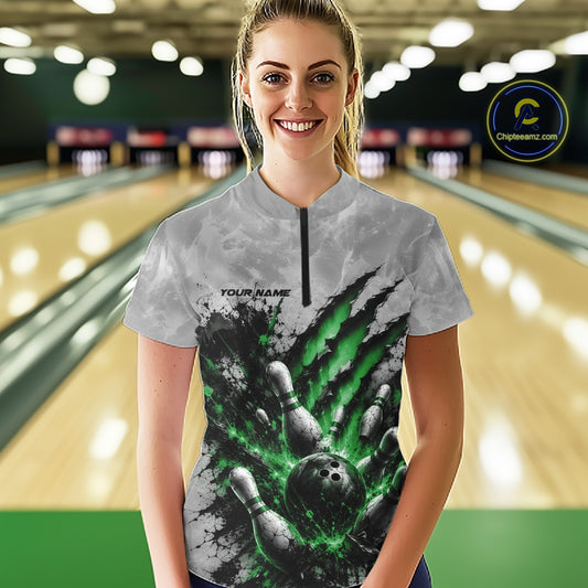 Front view of a female model wearing a gray bowling quarter zip shirt showcasing a dramatic green bowling ball and pins graphic with claw-mark artwork in a bowling lane.