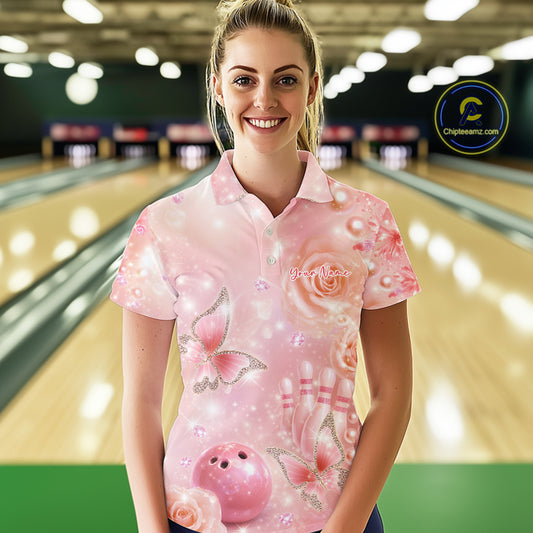 Female model at a bowling lane wearing a polo shirt with pink glitter butterflies, diamond details, bowling pins, and a bowling ball motif.