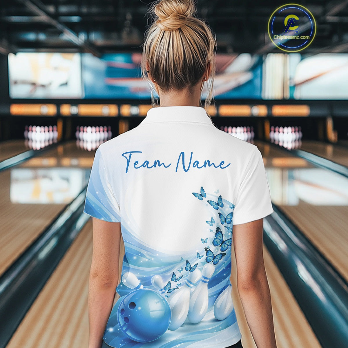 Back view of a women s white and blue bowling quarter zip showcasing butterfly artwork and bowling-themed graphics at the bowling lane.