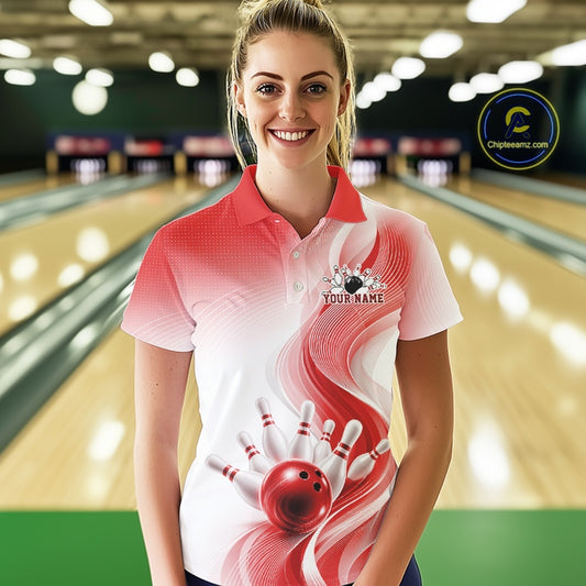 Female model wearing a white and red bowling polo with flowing abstract wave lines and a glossy bowling ball striking pins, front view inside a bowling center