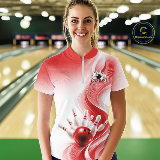 Female model in a white and red bowling quarter zip with flowing wave artwork and glossy bowling strike graphics, front view at the bowling lane