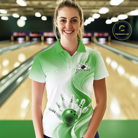Female model wearing a white and green bowling polo with flowing abstract wave graphics and a glossy bowling ball striking pins, front view at the bowling lane