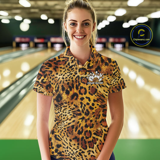 Smiling woman in a bowling alley wearing a gold, brown, and black leopard-print bowling polo with a small bowling pins graphic and “Your Name” on the chest.
