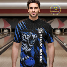 Load image into Gallery viewer, Male model wearing a black and mid blue bowling quarter-zip shirt in a bowling lane, displaying a roaring tiger holding a mid blue bowling ball with coordinated claw-stripe graphics and a geometric background pattern.