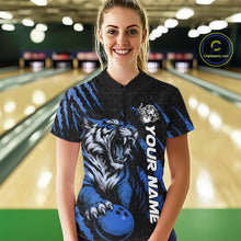 Load image into Gallery viewer, Front view of a female model at a bowling lane wearing a black and mid blue bowling quarter-zip shirt featuring a roaring tiger holding a mid blue bowling ball with coordinated claw-stripe graphics and a geometric background pattern.