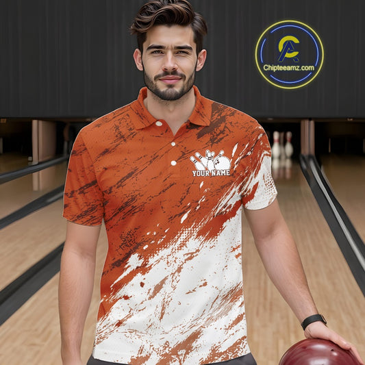 Front view of a male model in a bowling alley wearing a bowling polo shirt featuring a white paint splatter distressed sportswear design on an orange shirt.
