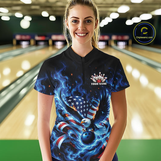 Front view of a female model in a bowling lane wearing a bowling quarter zip shirt with flaming eagle motif, blue bowling ball, and flag details.