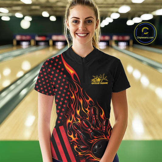 Female model at a bowling lane wearing a black bowling quarter-zip shirt with red-orange flame bowling strike artwork and American flag details.