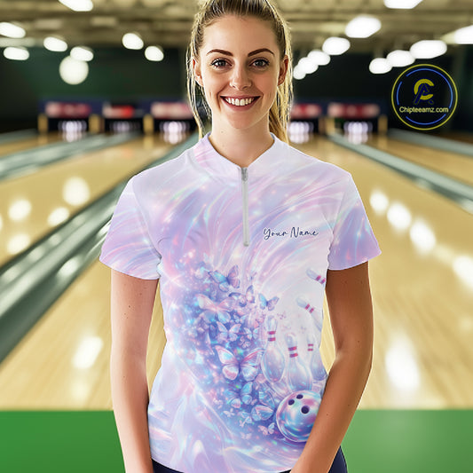 Female model wearing a bowling quarter zip with pastel holographic butterfly artwork and bowling graphics, front view inside a bowling alley