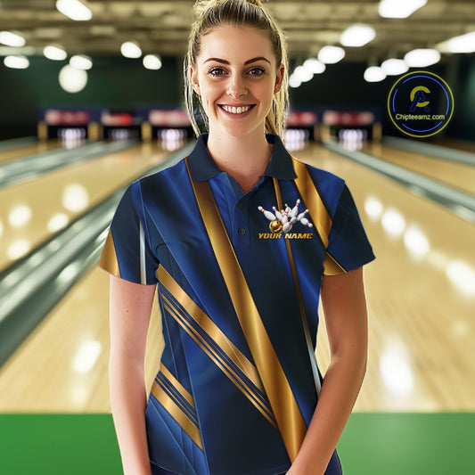 A woman standing in a bowling alley wearing a blue and gold bowling shirt with a white bowling pins graphic on the chest. The background shows blurred bowling lanes and lights.
