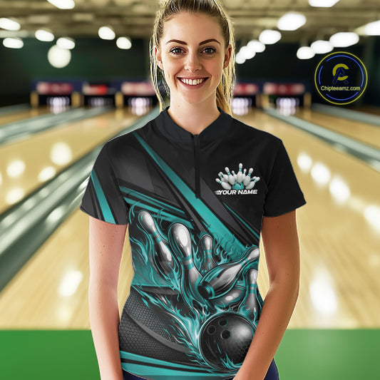 Female model in a bowling lane wearing a black quarter-zip shirt, turquoise flame bowling ball hitting pins with modern geometric stripe design.