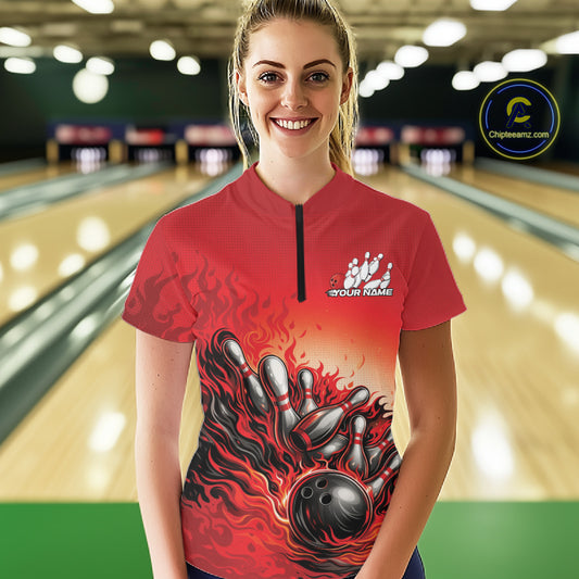 Female model in a bowling lane wearing a red quarter-zip shirt, flame bowling ball striking pins with energetic fire-style artwork.
