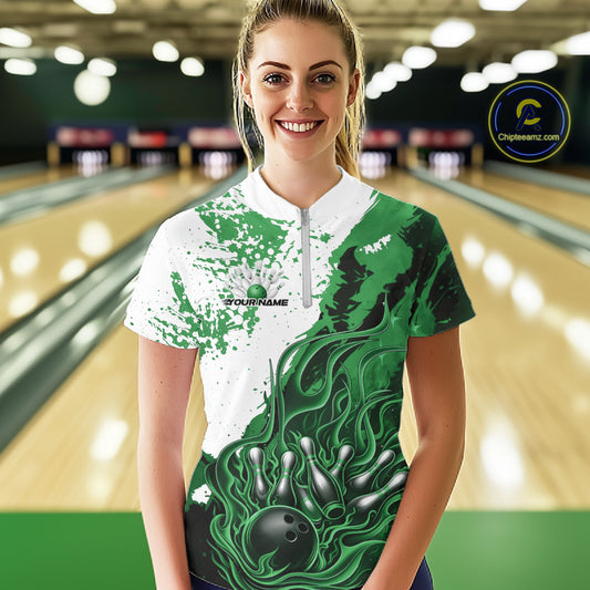 Front view of a female model in a bowling lane wearing a black, green and white flame bowling quarter-zip shirt with energetic bowling action graphics.