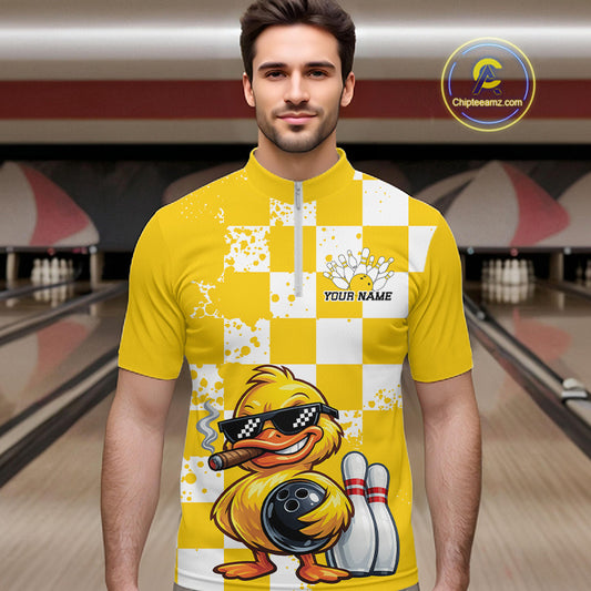 A man wearing a yellow and white checkered bowling-themed quarter-zip shirt with a cartoon duck graphic, set against a blurred bowling alley background. A 'Chipeezm.