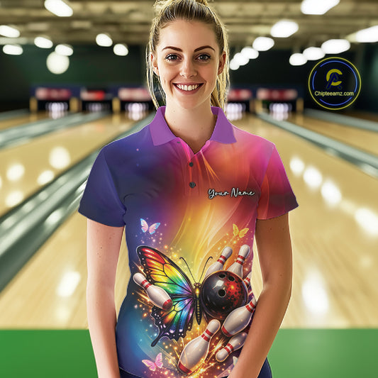 Female model at a bowling lane wearing a bowling polo shirt with a rainbow butterfly, bowling ball, and scattered pin artwork.