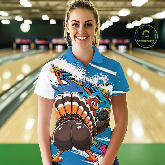 Front view of a female model wearing a blue custom bowling polo shirt with a funny graffiti turkey holding a bowling ball, paint splatter accents, and a personalized name in a bowling alley.