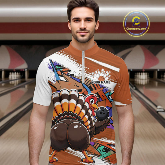 Front view of a male model wearing an orange custom quarter zip bowling shirt with a funny graffiti turkey holding a bowling ball, paint splatter accents in a bowling alley.