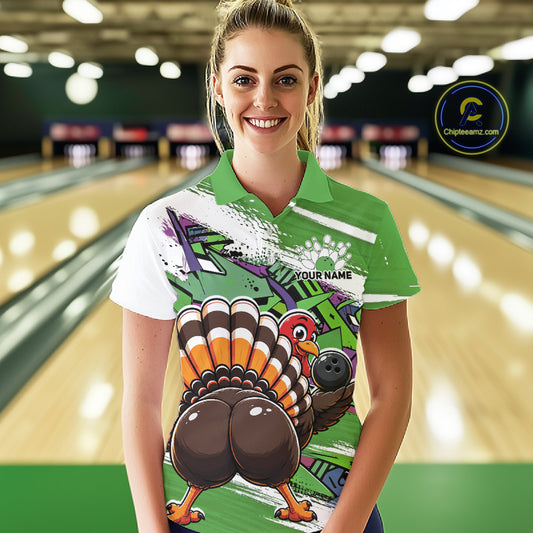 Front view of a female model wearing a green custom bowling polo shirt with a funny graffiti turkey holding a bowling ball, paint splatter accents, and a personalized name in a bowling alley.