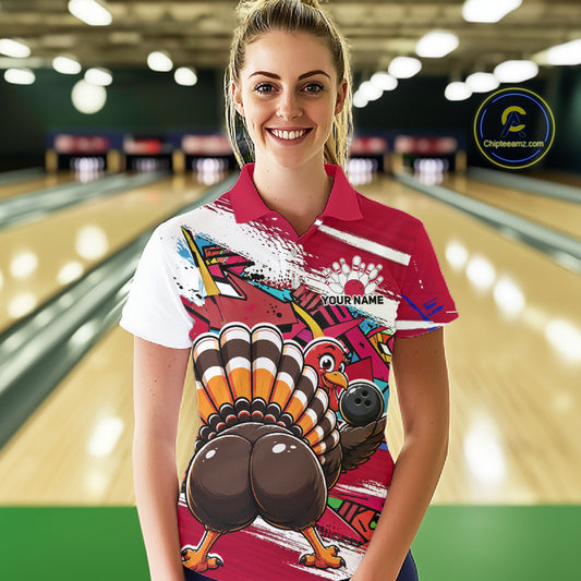 Front view of a female model wearing a red custom bowling polo shirt with a funny graffiti turkey holding a bowling ball, paint splatter accents, and a personalized name in a bowling alley.