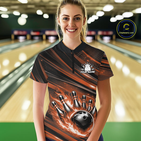 Female model in a bowling lane wearing black and orange quarter zip shirt, front view featuring fiery bowling ball hitting pins bold artwork