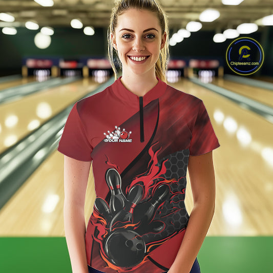 Female model in a bowling lane wearing a black and red quarter zip shirt, front view featuring flaming bowling ball hitting pins with hexagon accents