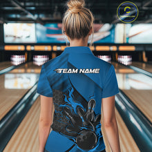 Load image into Gallery viewer, Back view of a female model in a bowling alley wearing a black and blue polo shirt featuring a flaming bowling ball knocking down pins.