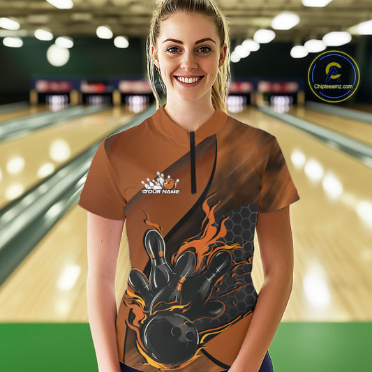 Female model in a bowling lane wearing black and orange quarter zip shirt, front view featuring flame bowling ball hitting pins dynamic artwork