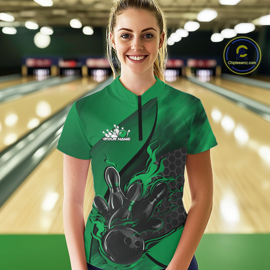 Female model in a bowling lane wearing black and green quarter zip shirt, front view featuring flaming bowling ball striking pins with hexagon design