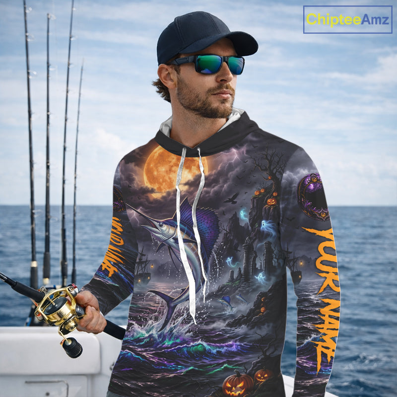 A man wearing a black baseball cap and sunglasses stands on a boat holding a fishing rod, wearing a long-sleeve hoodie with an all-over Halloween-themed graphic print featuring a fish, a ghost ship, jack-o'-lanterns, and orange text on the sleeves.