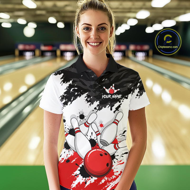 A woman stands in a bowling alley wearing a custom bowling-themed polo shirt. The shirt features a black and white splatter design with a red bowling ball graphic and the text 'YOUR NAME' and 'CHOOSE A NAME'.