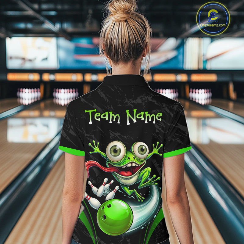 A woman viewed from behind wearing a black bowling-themed short-sleeve polo shirt with a colorful cartoon frog graphic and the text 'Team Name' on the back. The background shows blurred bowling alley lanes and pins.