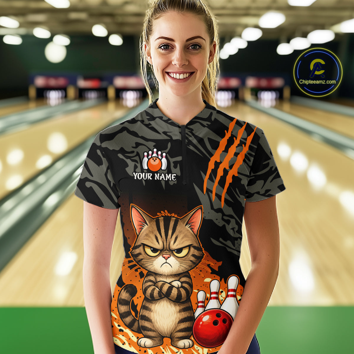 A woman stands in a bowling alley wearing a custom bowling shirt with a black tiger-stripe pattern, orange claw marks, a cartoon grumpy cat, and a red bowling ball graphic. A 'Championship.