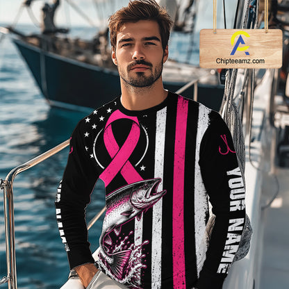 A man wearing a long-sleeve custom graphic shirt on a boat, featuring a black and white distressed American flag design with a pink ribbon, a salmon fish graphic, and 'YOUR NAME' printed on the sleeve.