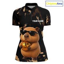 Load image into Gallery viewer, Polo shirt with a capybara design holding a gold ball on a black background, featuring the brand 'ChipteeAmz'.
